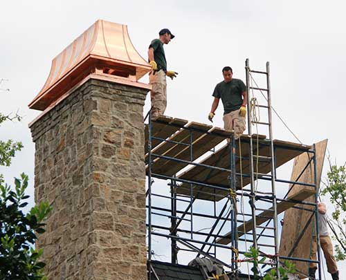 Technicians on scaffolding working on a custom copper chimney cap install
